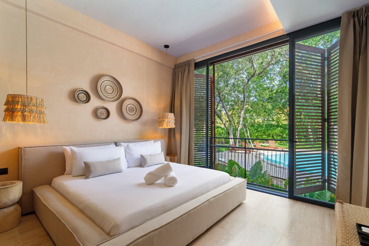 Ein modernes Hotelzimmer mit einem großen Bett, Blick auf einen Pool und einem Balkon mit Ausblick ins Freie.