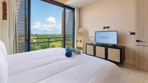 Habitación de hotel con una cama grande, un televisor sobre un mueble y vistas a zonas verdes por la ventana.