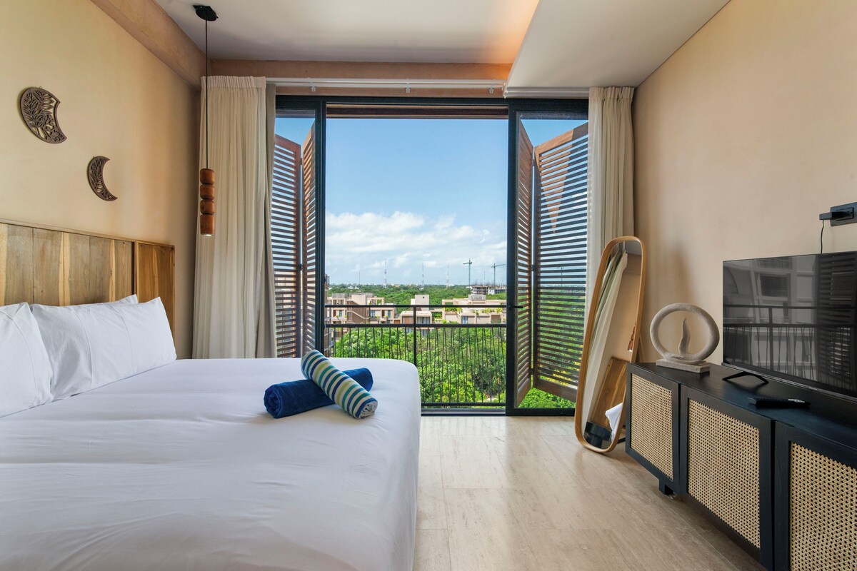 Ein Hotelzimmer mit Bett, Fernseher und Balkon mit Blick auf Gebäude.