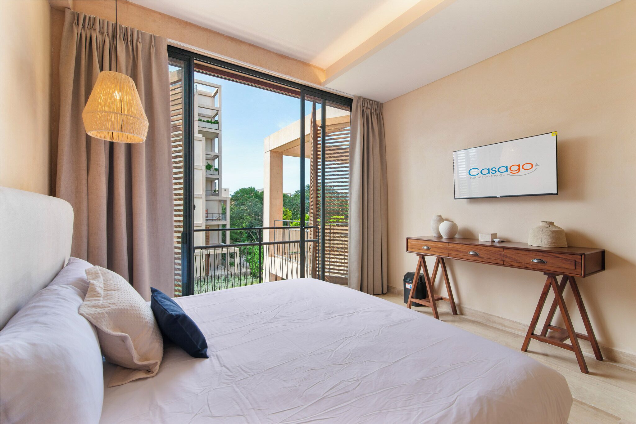 Une chambre d’hôtel avec un grand lit, un bureau, une télévision et un balcon donnant sur un paysage verdoyant.