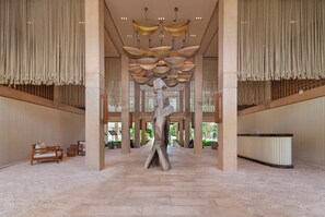 Eine großzügige Lobby mit einer zentralen Skulptur, hohen Decken und einer Rezeption.