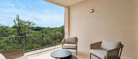 A balcony with wicker furniture, a round table, and a view of greenery.