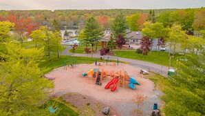 A playground with slides and climbing structures, surrounded by trees and a road. - Lake Monster Family Adventure! Kayak fishing Firepit Hot tub Sauna Games & More (Tobyhanna)
