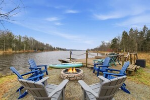 A lakeside deck with Adirondack chairs, a fire pit, and a kayak. - Lake Monster Family Adventure! Kayak fishing Firepit Hot tub Sauna Games & More (Tobyhanna)