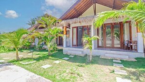A modern house with a thatched roof, large windows, and a well-maintained garden with palm trees. - Kalpataru Cottage (Bali)