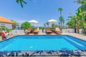 Une piscine entourée de plantes tropicales, avec des chaises longues et des parasols.