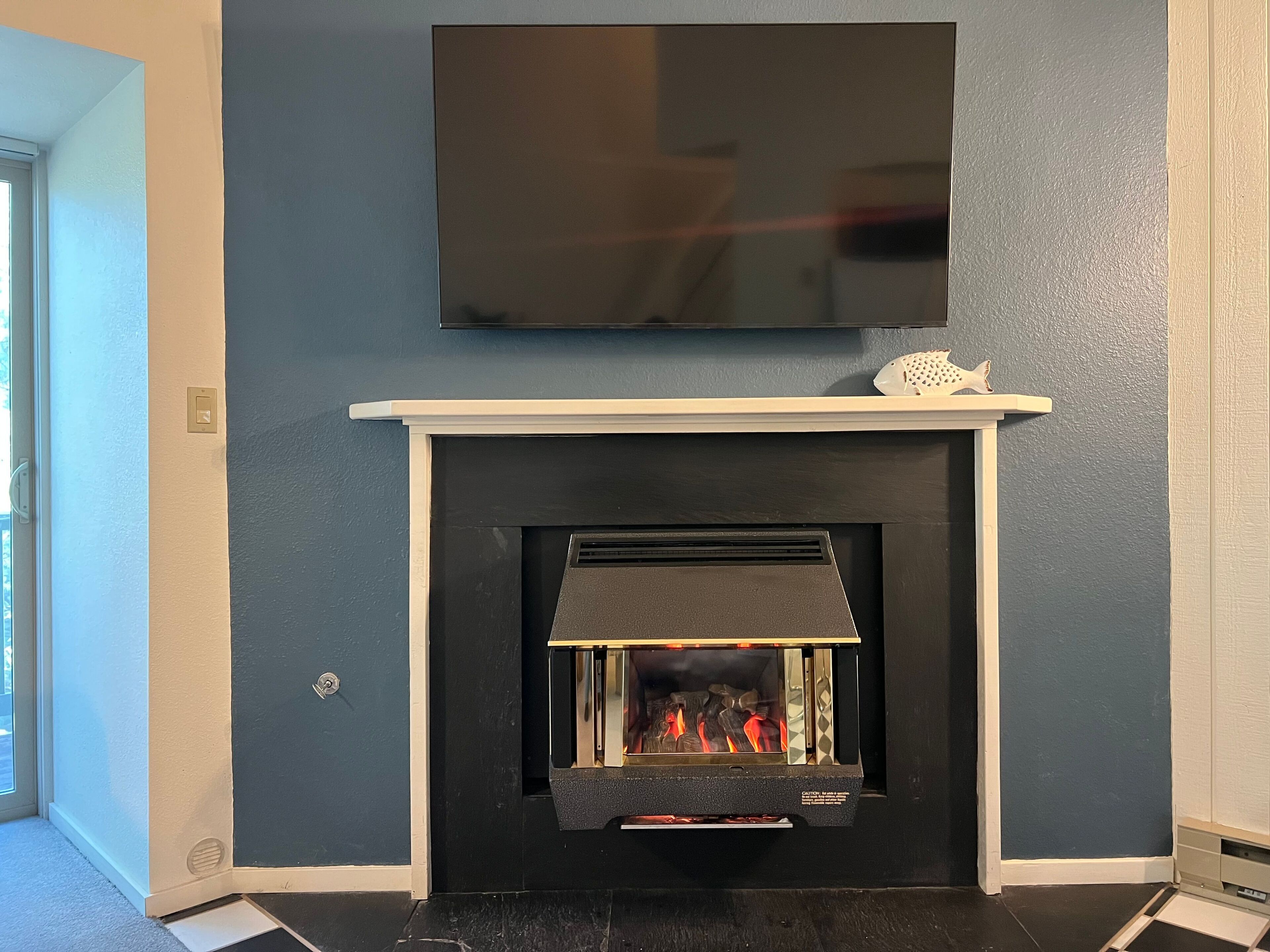 A modern living room with a fireplace, a flat-screen TV mounted above it, and a decorative item on the mantel.