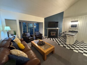 Ein Wohnzimmer mit braunem Ledersofa, zwei Sesseln, einem Holztisch und einem Kamin.