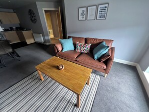 A living room with a brown leather sofa, a wooden coffee table, and a striped rug. There are three framed pictures on the wall. - 2 bedroomed executive apartment (Cleethorpes)