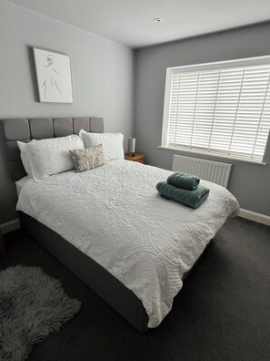 Une chambre à coucher avec une tête de lit rembourrée de couleur grise, une couvre-lit blanche à texture particulière et un tapis gris à poils longs.