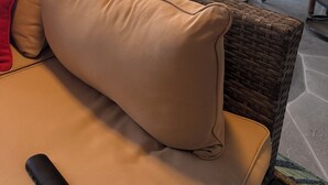 A wicker sofa with a beige cushion and a red pillow, a glass table, and a pool area with colorful lounge chairs. - 3 bedroom Amazing cool house with tons of character! (Port Charlotte)