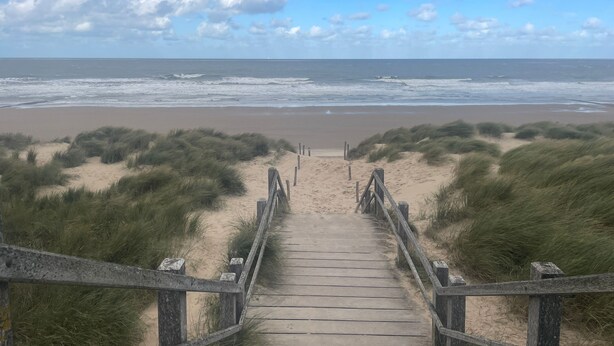 A wooden boardwalk leading to a beach with dunes and the ocean in the background.