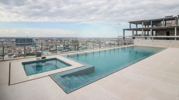 Una piscina infinita en la azotea con vistas a la ciudad, una piscina más pequeña aparte y una estructura de edificio moderna.