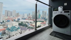 Habitaci ón en un edificio alto con un ventanal grande que da a una vista urbana, incluyendo una mezquita y varios edificios. Hay dos unidades de aire acondicionado fijadas a la pared y una lavadora.