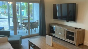 Un soggiorno con divano, tavolino, TV a parete e una porta scorrevole in vetro che dà su uno spazio esterno.