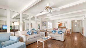 A spacious living room with a sofa, armchair, and coffee table, a kitchen in the background, and a ceiling fan. - 2BR Family Condo at Tropical Sands (Fort Myers Beach)