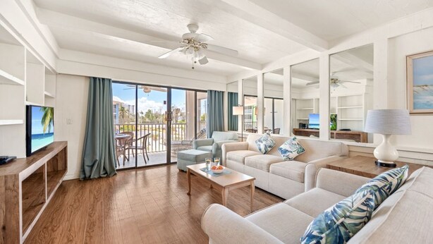 A spacious living room with a balcony, a ceiling fan, and a television. - 2BR Family Condo at Tropical Sands (Fort Myers Beach)