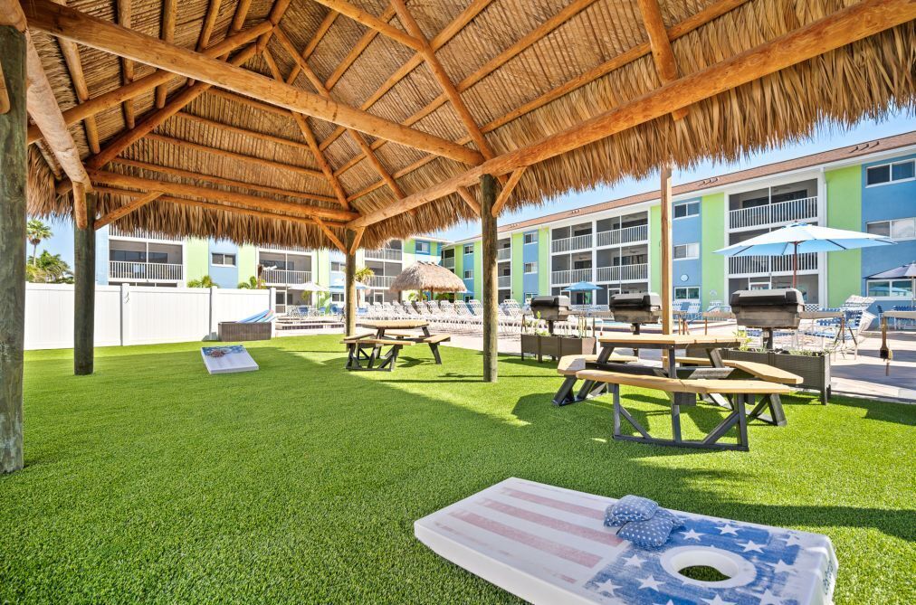 A covered outdoor area with picnic tables, lounge chairs, and a pool in the background.
