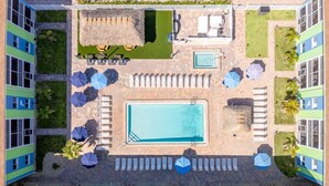 Ein Luftbild eines Hotels mit Schwimmbecken, Liegestühlen und einem strohgedeckten Bereich.