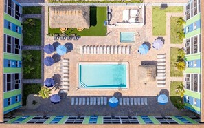 Ein Luftbild eines Hotels mit Schwimmbecken, Liegestühlen und einem strohgedeckten Bereich.