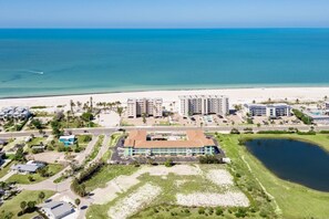 Luftaufnahme eines Küstenhotels mit mehreren Gebäuden, einem Strand und einem Parkplatz.