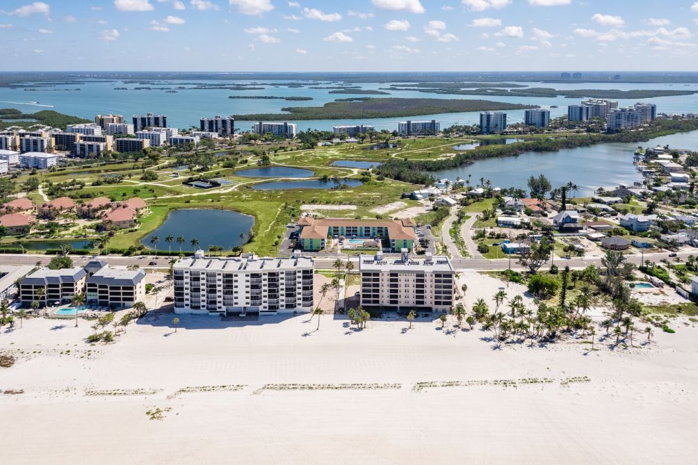 Un complejo turístico costero con varios edificios altos, una playa y un puerto deportivo.