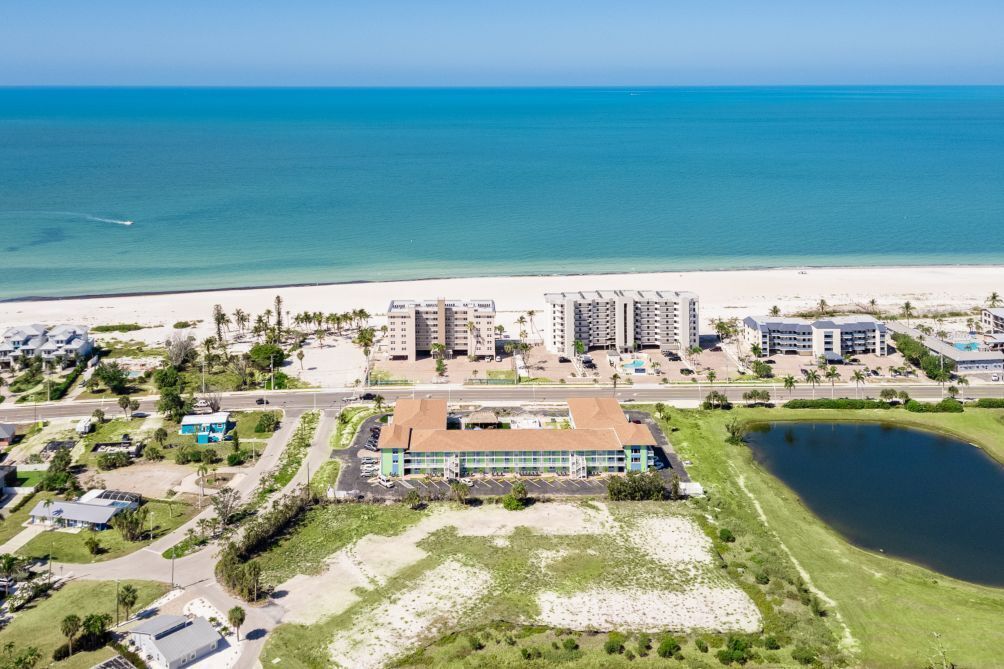 An aerial view of a coastal hotel with multiple buildings, a beach, and a parking lot.