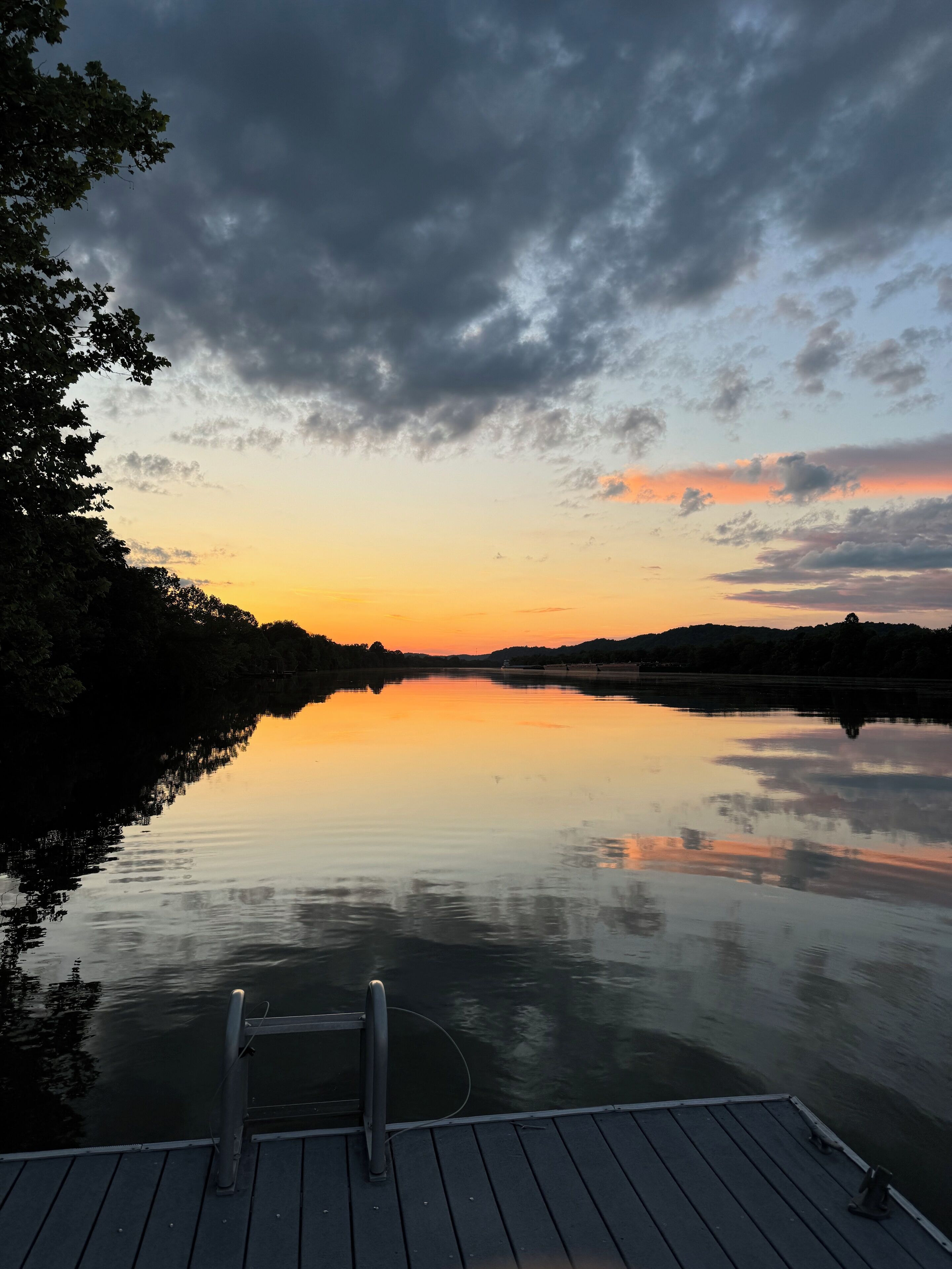 A calm lake at sunset with a wooden dock in the foreground.