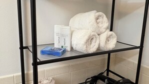 Een zwarte metalen plankenunit met handdoeken, toiletartikelen en een zwarte tas.