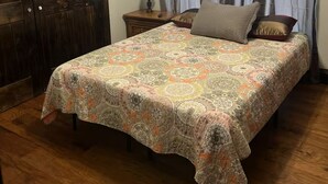Un dormitorio con puerta de madera, cama con colcha estampada, mesita de noche con lámpara y ventana con cortinas.