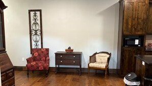 Una habitación amplia con suelo de madera, un armario de madera, un sillón rojo, una mesita pequeña y un adorno de pared.