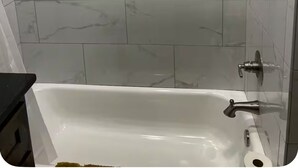 Un baño con pared de blanco mármol, un estante empotrado con dos botellas y una bañera blanca con grifo.