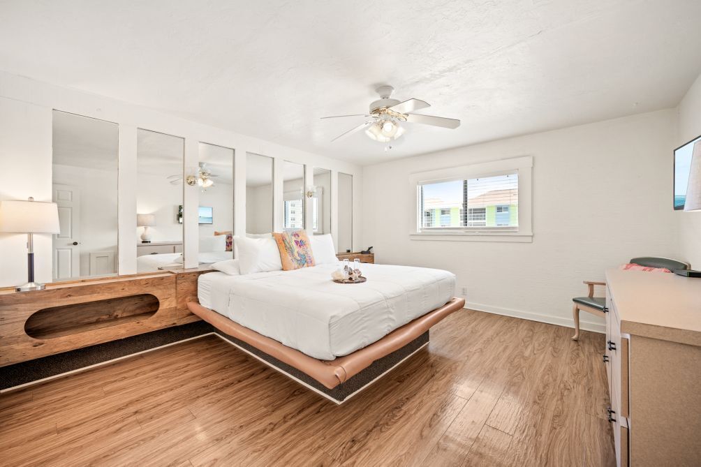 A bedroom with a bed, a ceiling fan, a window, and a desk.