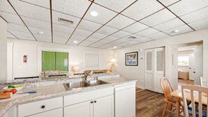 Une cuisine avec des meubles blancs, un plan de travail en granit, un évier et un coin repas comprenant une table et des chaises en bois.