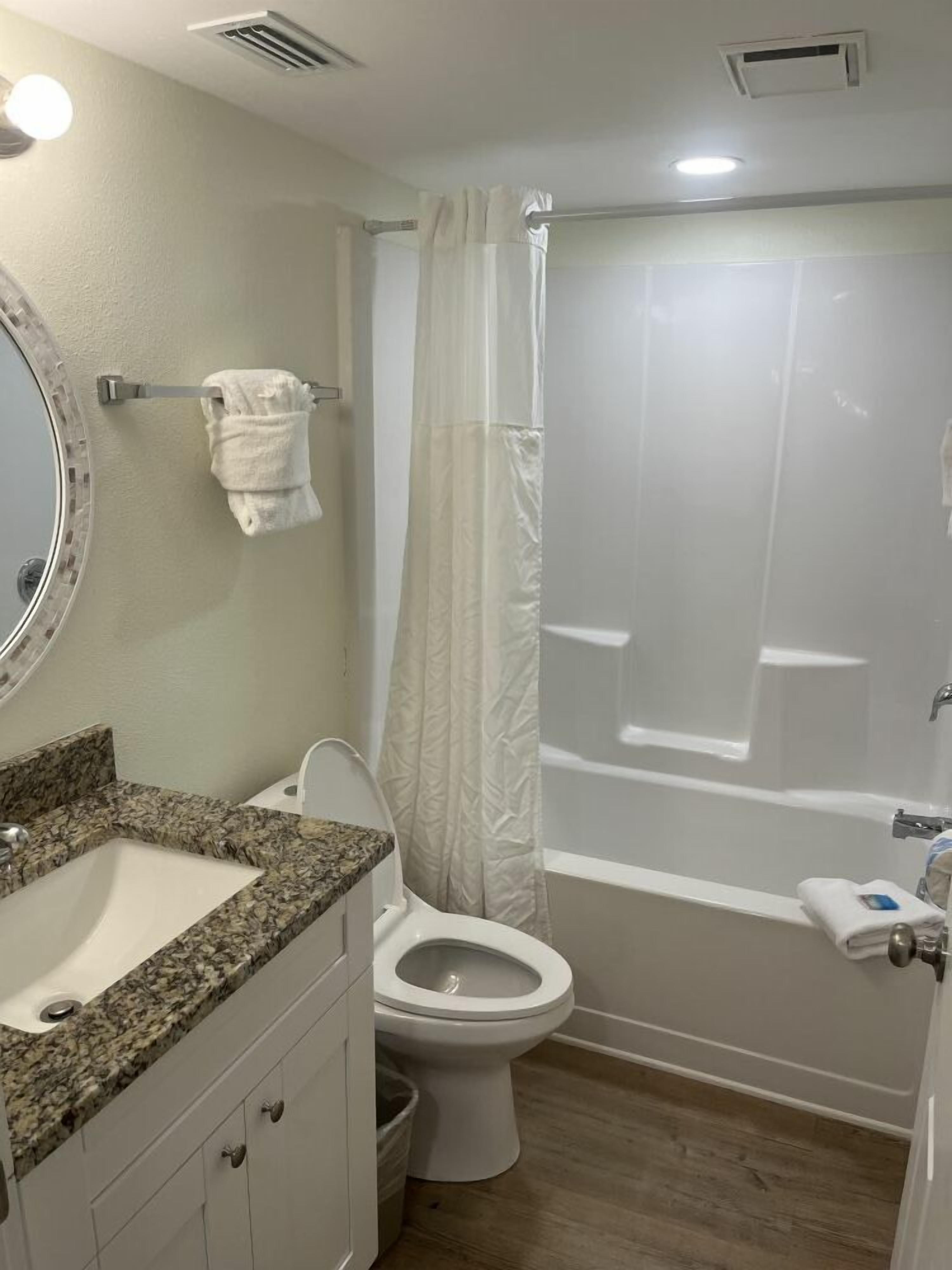 A bathroom with a granite countertop sink, a toilet, and a bathtub with a shower curtain.