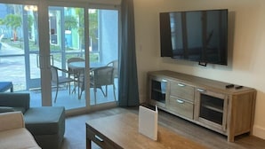 Uma sala de estar com sofá, mesa de centro, televisão fixada na parede e porta de vidro deslizante para área externa.