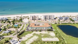 Vista aérea de um hotel à beira-mar, com vários edifícios, uma praia e um estacionamento.