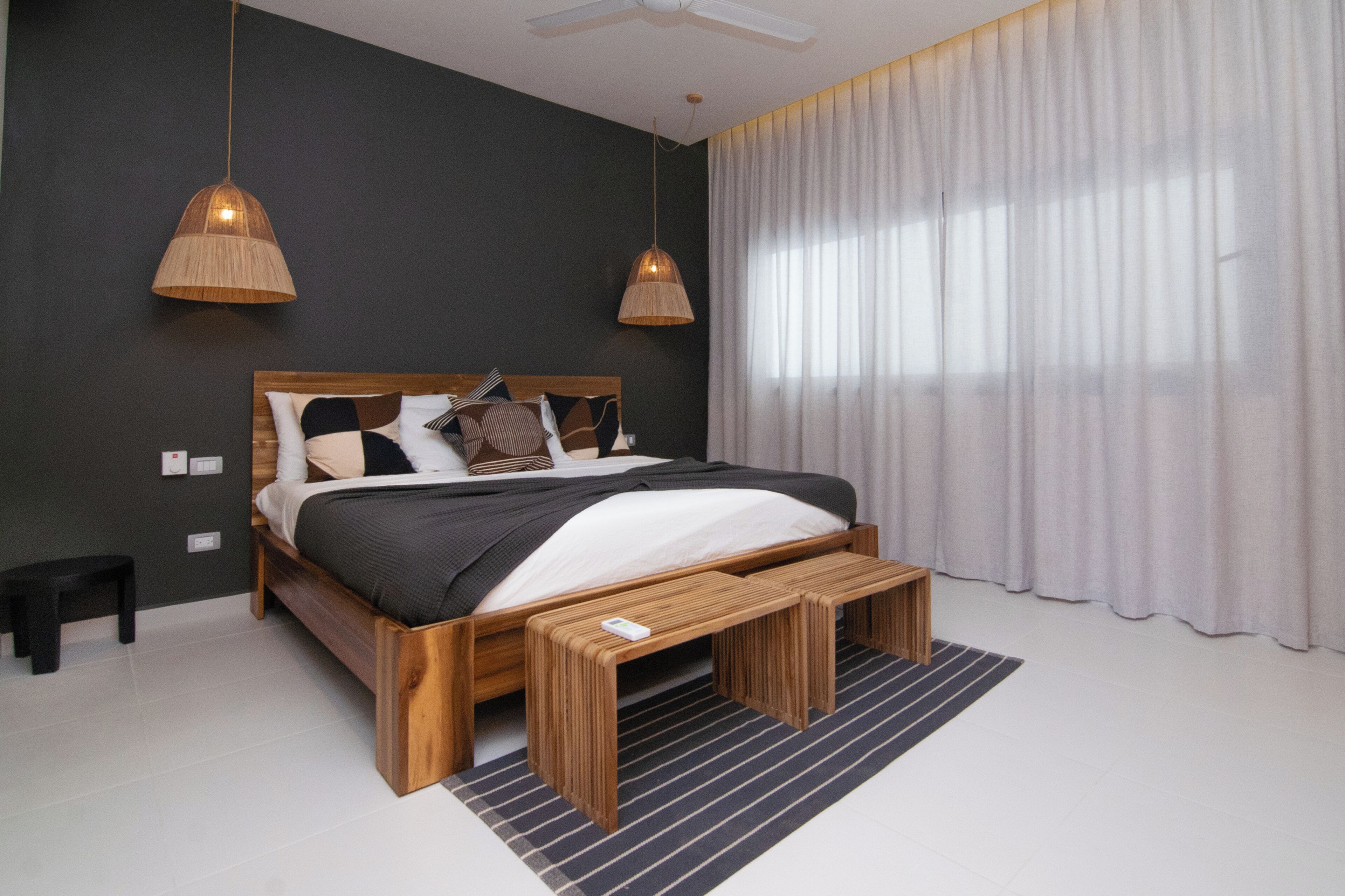 Ein modernes Schlafzimmer mit einem Holzbett, zwei Pendelleuchten, einer Bank und einem großen Fenster mit Vorhängen.