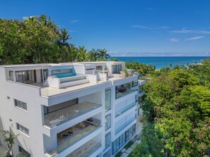 Un edificio moderno de varios pisos con piscina en la azotea, ventanas amplias y vista al océano.