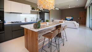 Een moderne keuken met een centraal eiland, barkrukken, een televisie en een plafondventilator.