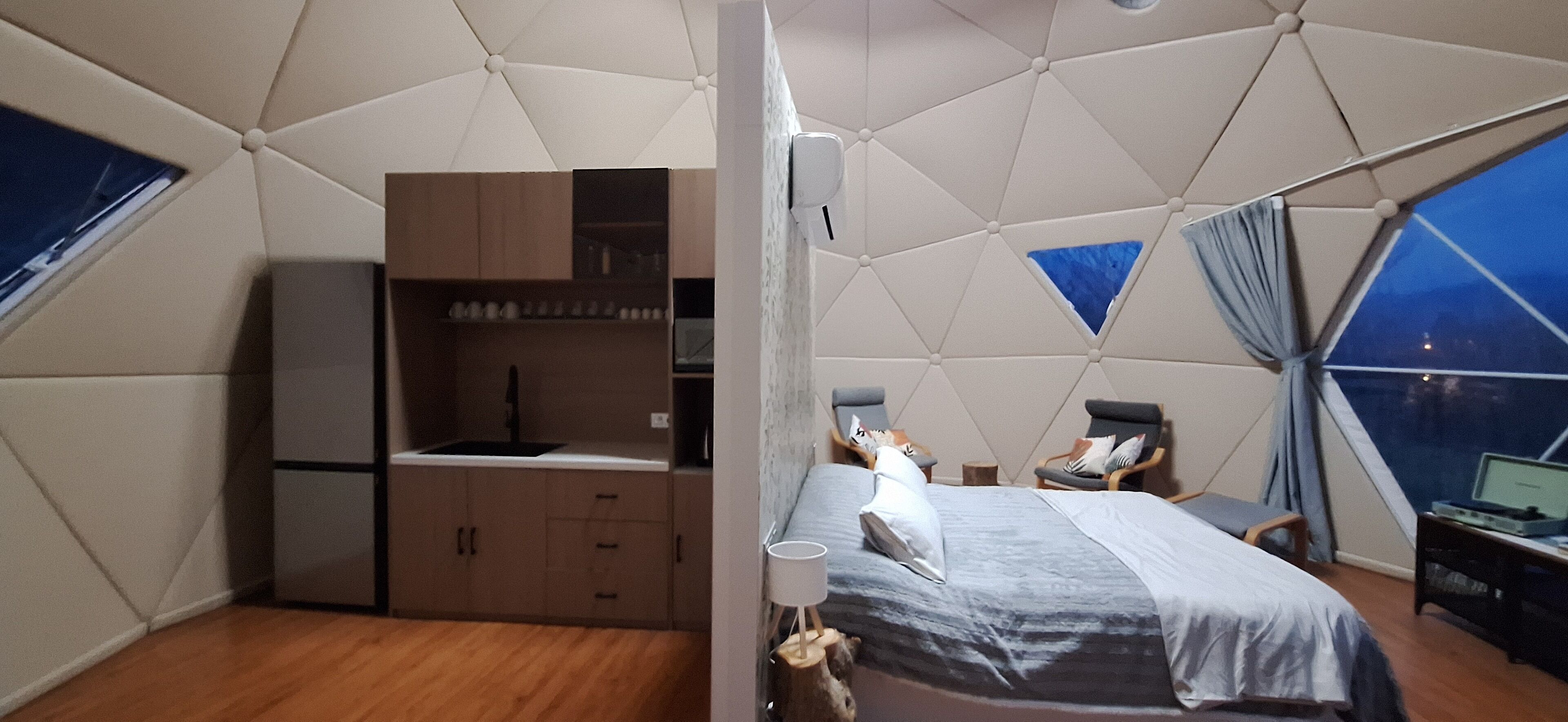 Un dormitorio con cama, escritorio y silla. Se ve una ventana con cortinas y vistas a la ciudad.