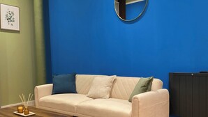 Un salon avec un mur bleu, un miroir rond, un canapé beige agrémenté de coussins, une table basse en bois et un tapis gris.