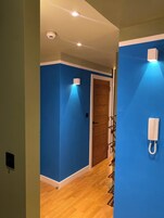 Un pasillo con paredes azules, suelo de madera, una puerta de madera y un teléfono blanco montado en la pared.