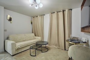 A room with a beige sofa, a small round table with a gold frame, and a chair. - Charming A/C Flat - Center of Paris - Le Marais (Paris)