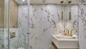 Ein modernes Badezimmer mit Duschkabine aus Glas, Marmorwänden, einem hölzernen Waschtisch und goldenen Armaturen.