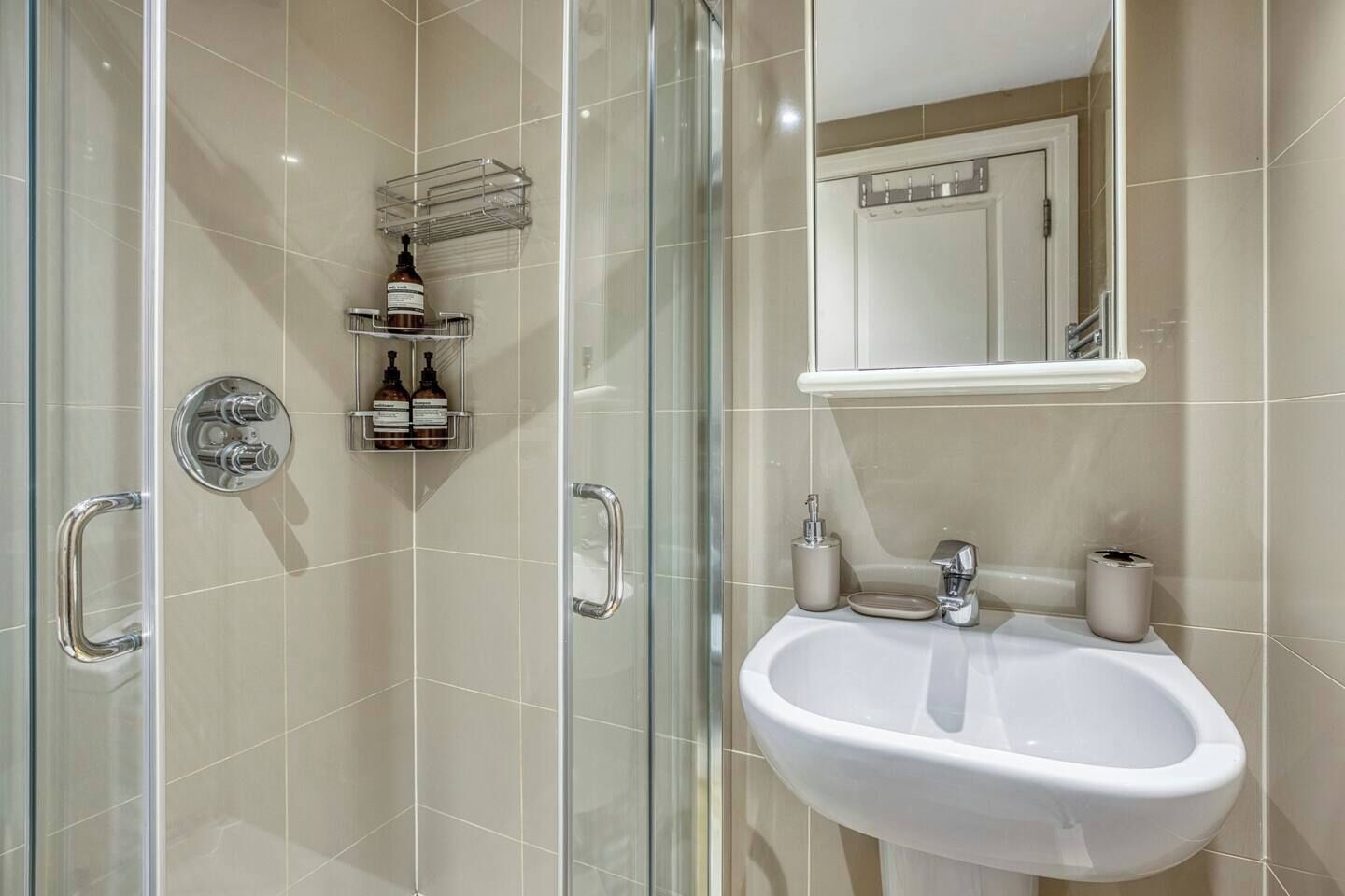 A modern bathroom with a glass-enclosed shower, a white sink with a mirror above it, and toiletries on the wall.