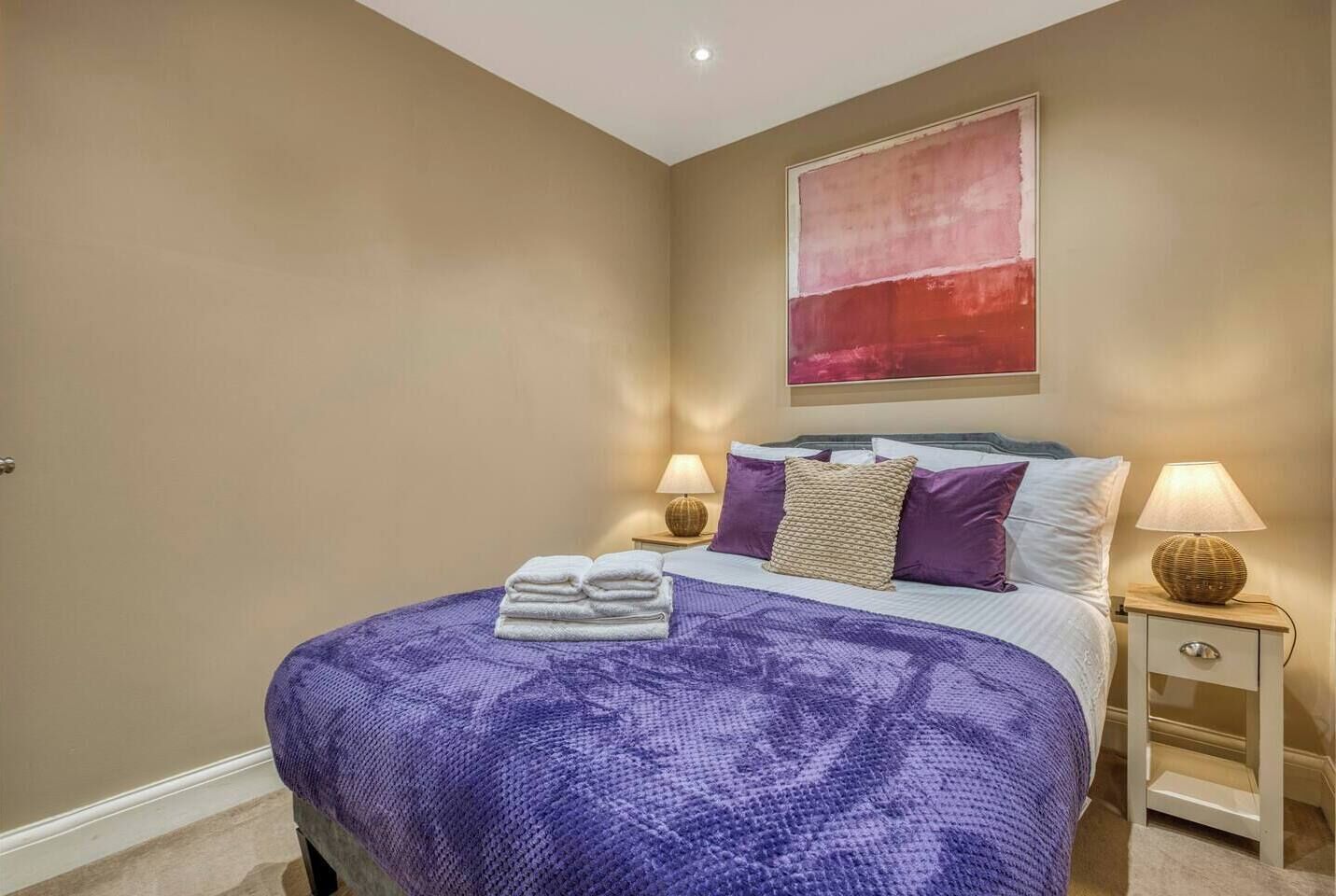 A bedroom with a large bed, two bedside tables, and a wall-mounted artwork.