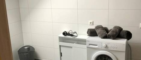 A laundry room with a washing machine, a drying rack, and a small basket.