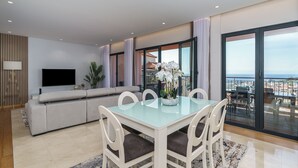 A modern living room with a glass dining table, white chairs, a grey sofa, and a flat-screen TV. - MAR E SOL: The ultimate Madeira escape with stunning views and modern comforts! (Funchal)