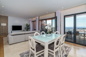 A modern living room with a glass dining table, white chairs, a grey sofa, and a flat-screen TV. - MAR E SOL: The ultimate Madeira escape with stunning views and modern comforts! (Funchal)